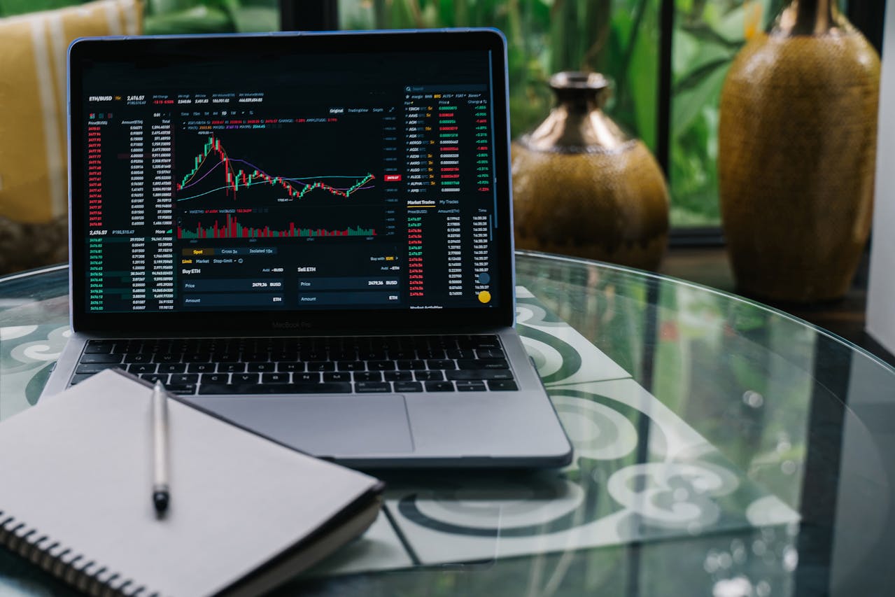 A laptop displaying investing charts next to a notebook