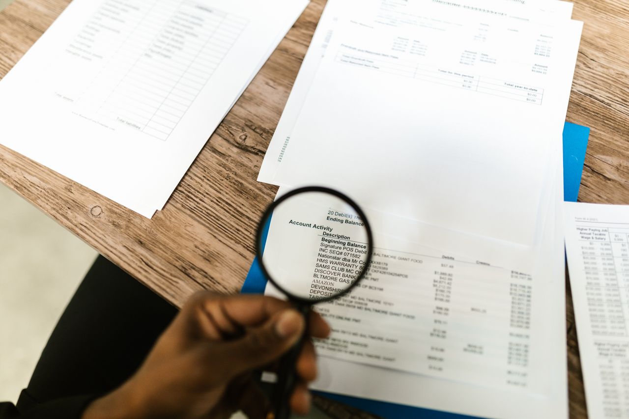 A person using a magnifying glass to look over documents to determine when to drop a merchant from your processing book